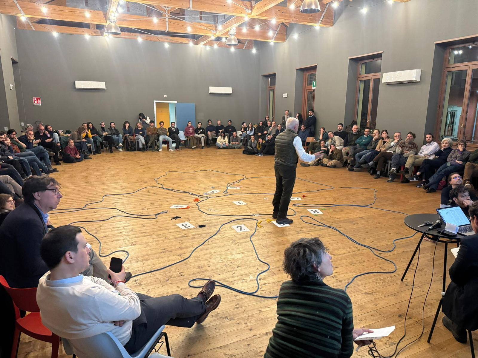 Un'agorà in una sala: le persone sedute in cerchio ascoltano chi parla